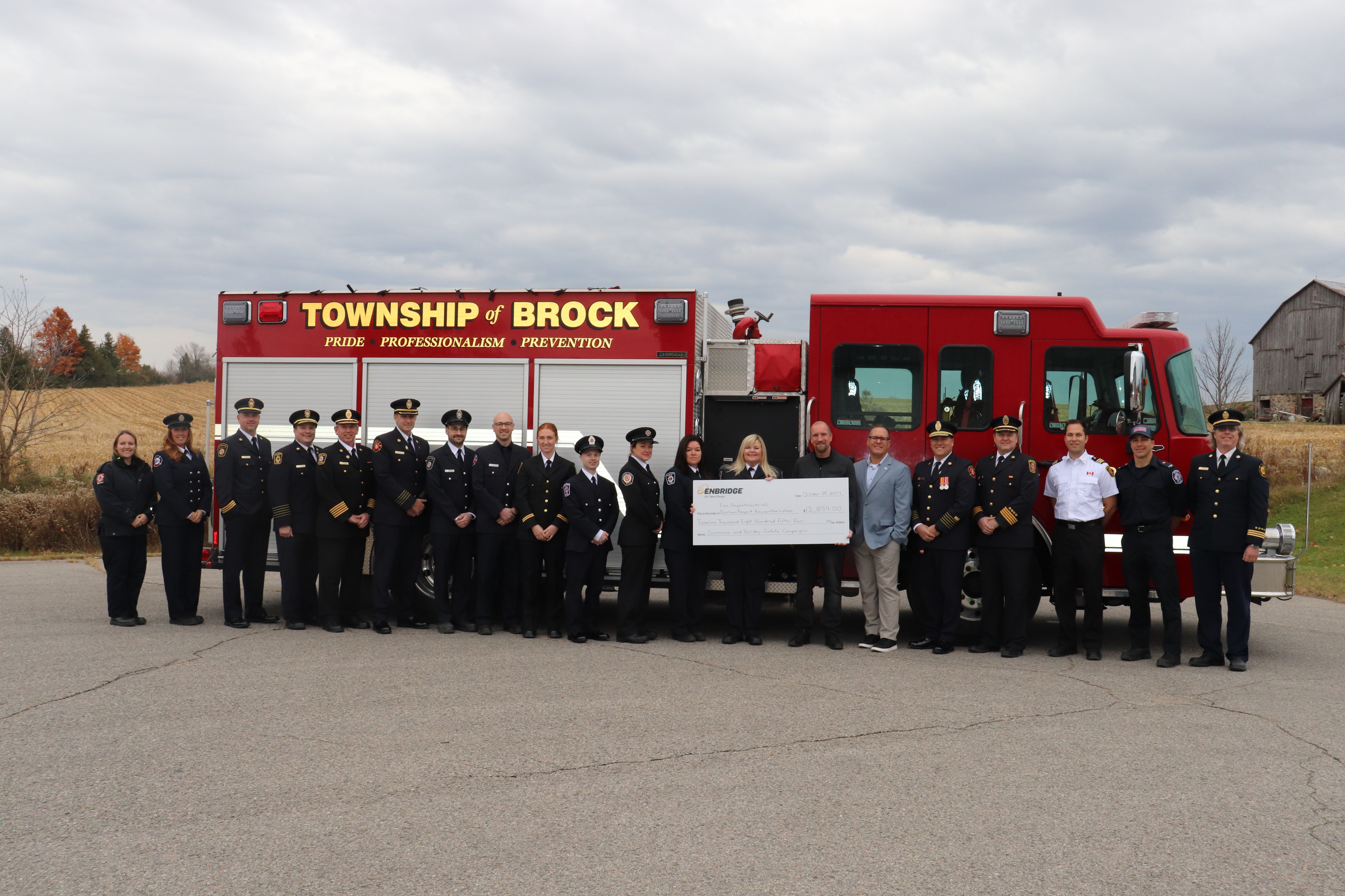 Durham fire chiefs and Fire Prevention Officers lined up with an endbridge cheque and a fire truck behind them